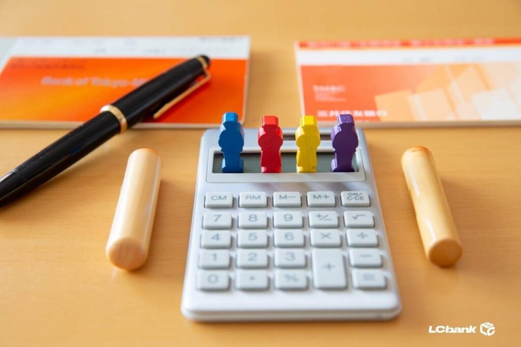 Calculadora com peças coloridas simbolizando pessoas, ao lado de itens bancários, representando organização financeira. Imagem LCbank.