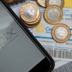 Celular com aplicativo Pix ao lado de moedas e boletos, representando o uso do dinheiro de precatórios e RPVs para quitar contas, resolver pendências financeiras e antecipar valores que o governo ainda não pagou.