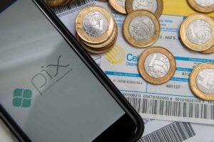 Celular com aplicativo Pix ao lado de moedas e boletos, representando o uso do dinheiro de precatórios e RPVs para quitar contas, resolver pendências financeiras e antecipar valores que o governo ainda não pagou.