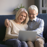 Casal sênior sorri assistindo laptop, protegendo direitos previdenciários